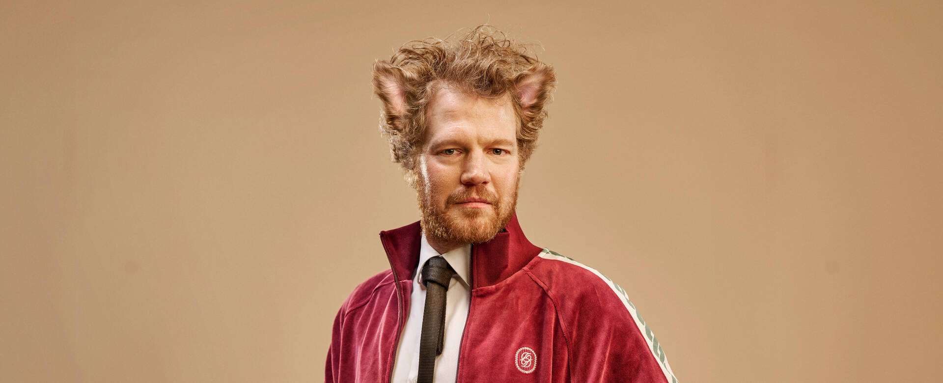 Man met een rode sportjack, stijlvolle uitstraling en kattenoren, tegen een neutrale achtergrond.