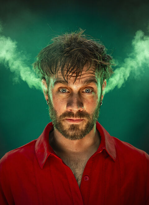 Portret van een man met een intense blik, omgeven door groene rook die uit zijn hoofd lijkt te komen.