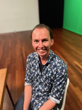 Jongen met een blije uitstraling, zittend op een stoel in een studio met een groene achtergrond.