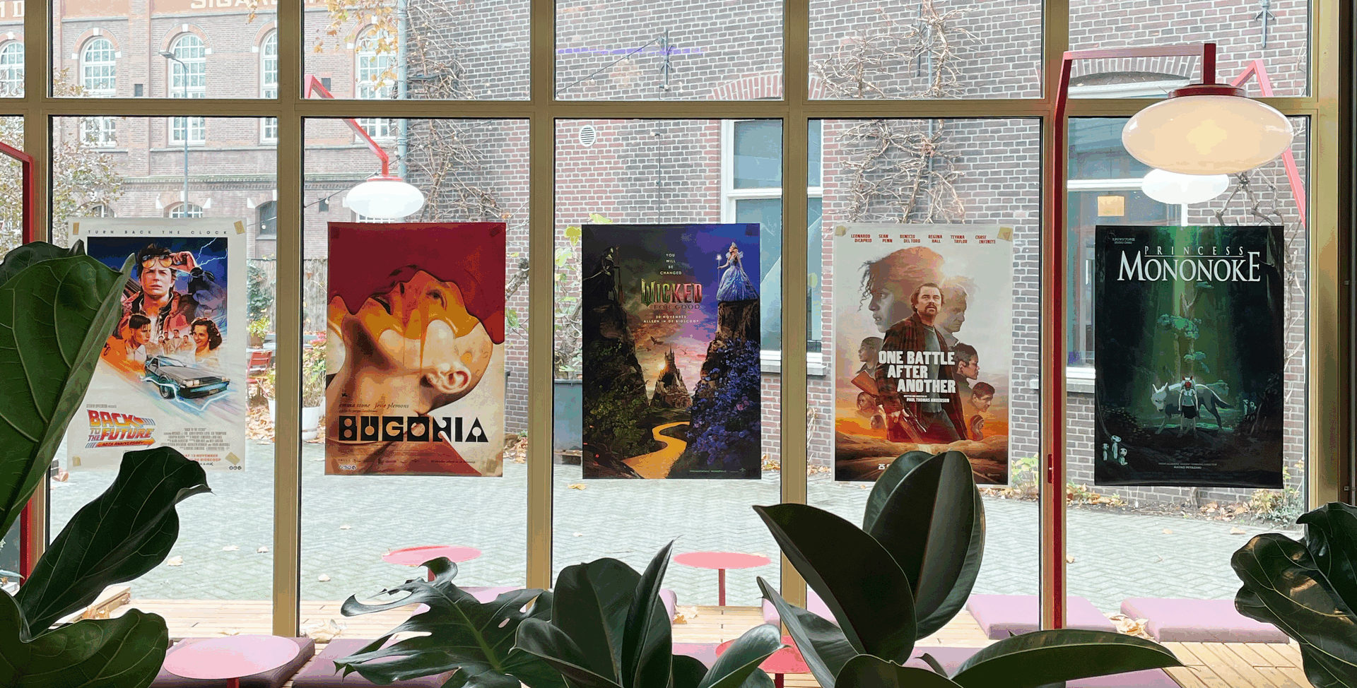 Kleurrijke filmposters hangen aan een raam, met zitplaatsen en planten op de voorgrond.