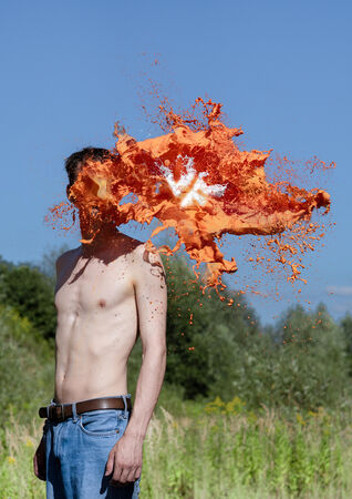 Een man met een bloot bovenlichaam die in een veld staat, met een explosie van oranje vloeistof die zijn hoofd vervangt.