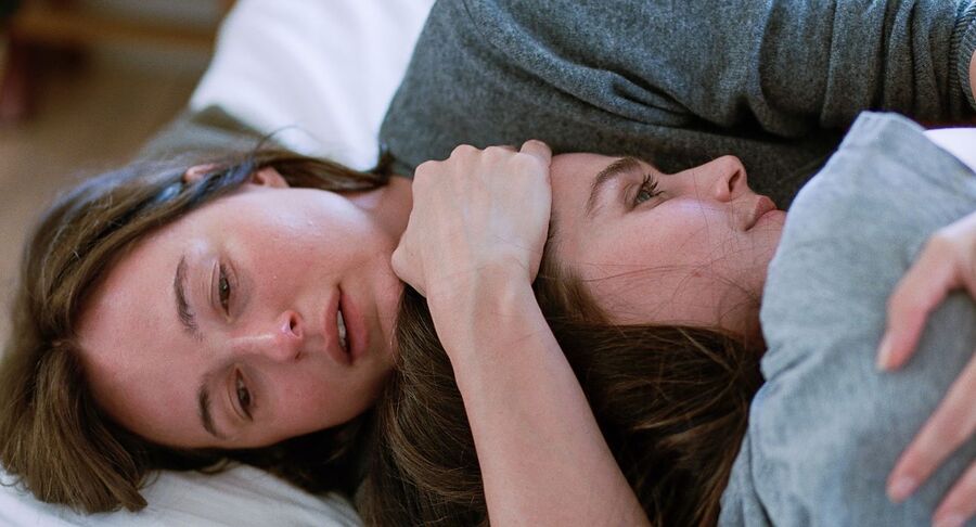 Twee vrouwen liggen samen op een bed, intiem en steunend in een emotioneel moment.