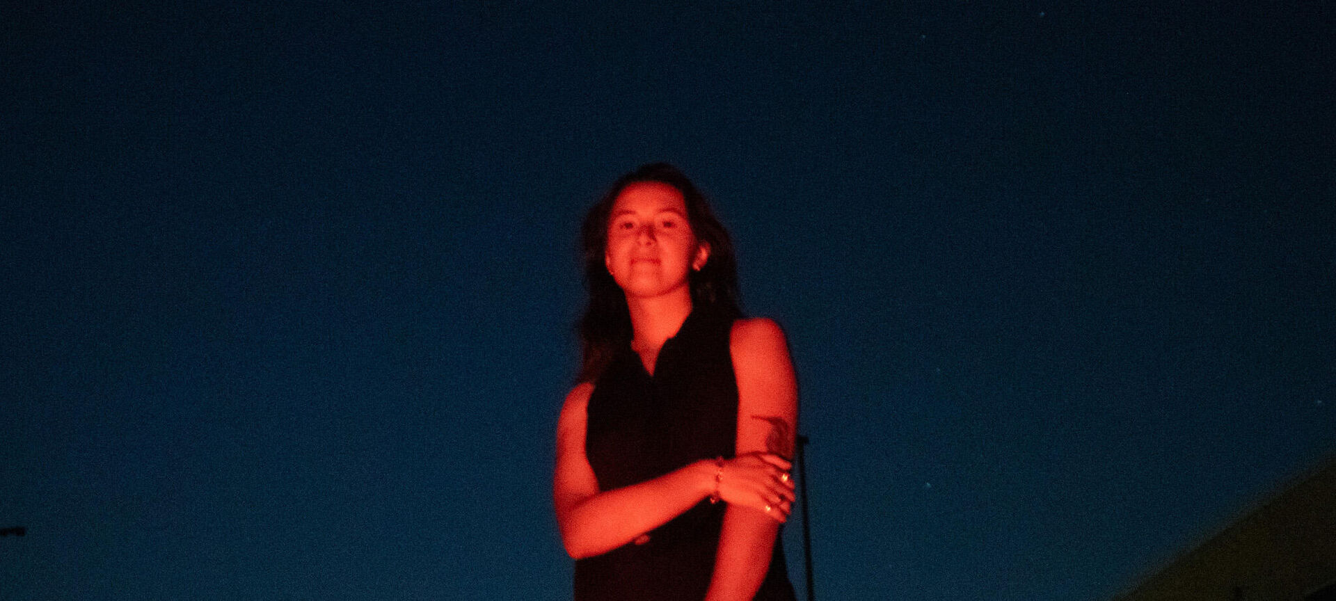 A woman stands in front of a building illuminated at night, showcasing the architecture against the dark sky.
