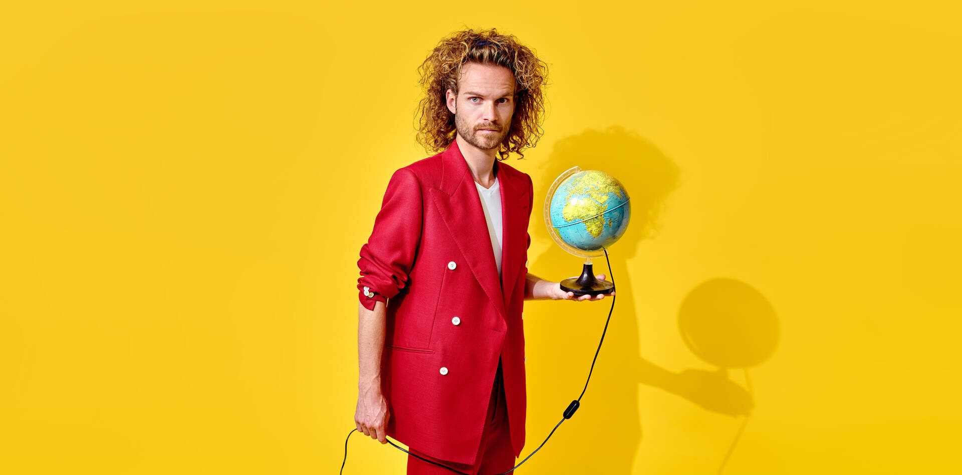 Man in een rode suit houdt een globe vast voor een heldergele achtergrond.