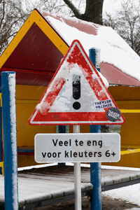 Waarschuwingsteken bij een speeltuin, met de tekst "Veel te eng voor kleuters 6+" in een sneeuwachtige omgeving.