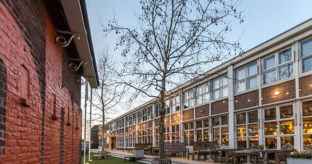 Moderne gebouwen met grote ramen, omringd door bomen en een grasgebied, onder een heldere lucht.