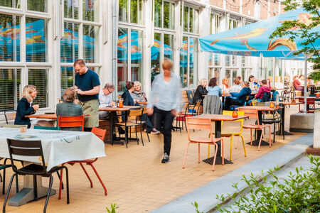 Drukke terrassen met mensen die genieten van hun tijd, omgeven door groene planten en kleurrijke parasols.
