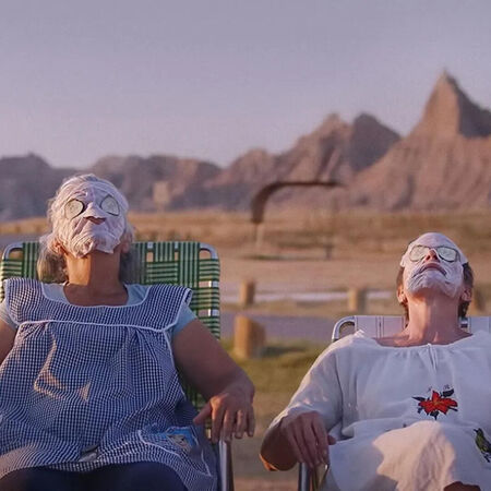 Twee vrouwen met gezichtsmaskers ontspannen in ligstoelen met bergen op de achtergrond.