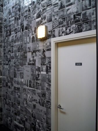 Een muur bedekt met zwart-wit foto’s en een deur met een naambordje ernaast.